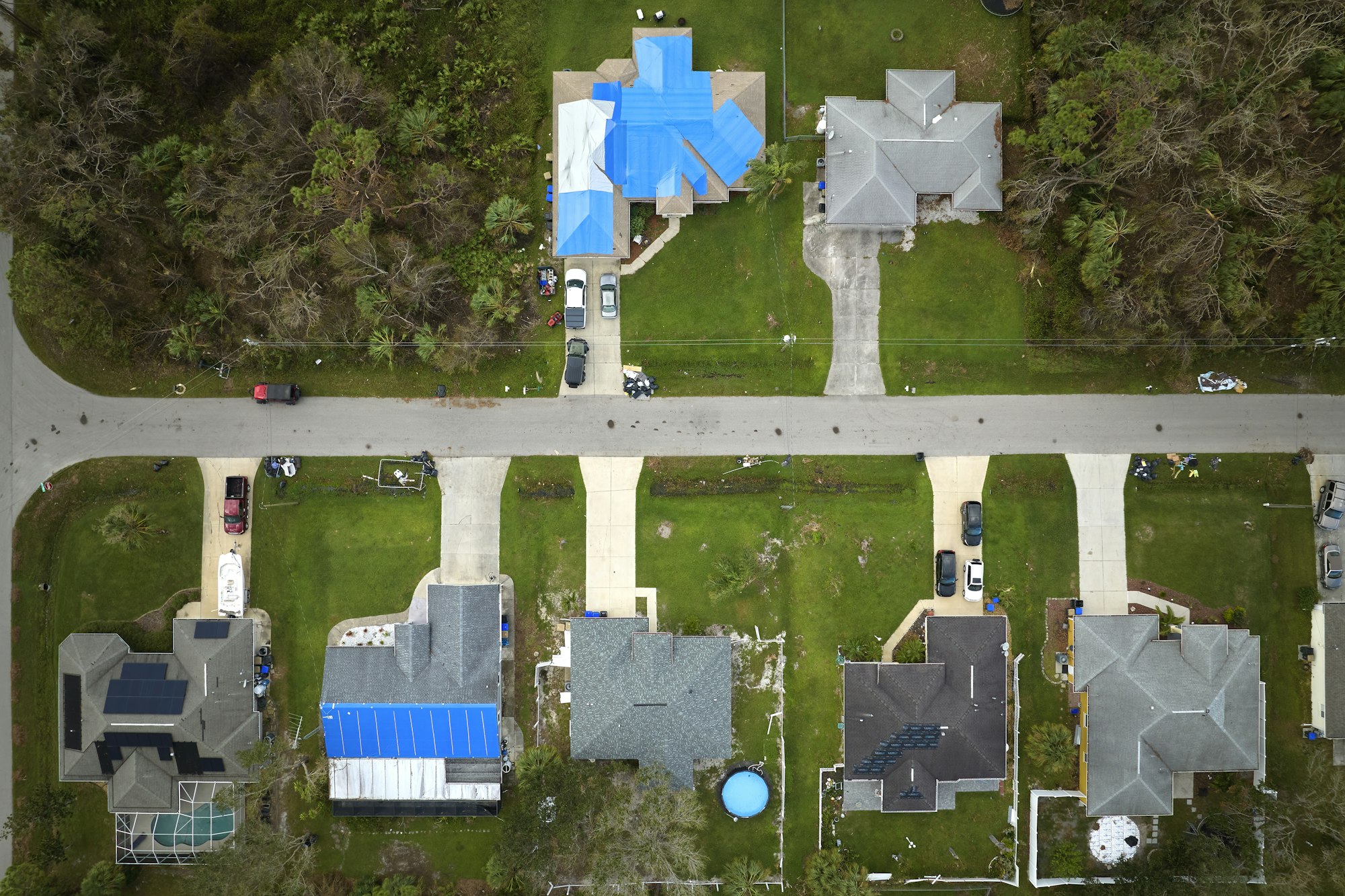 Aerial view of damaged in hurricane Ian house roof covered with blue protective tarp